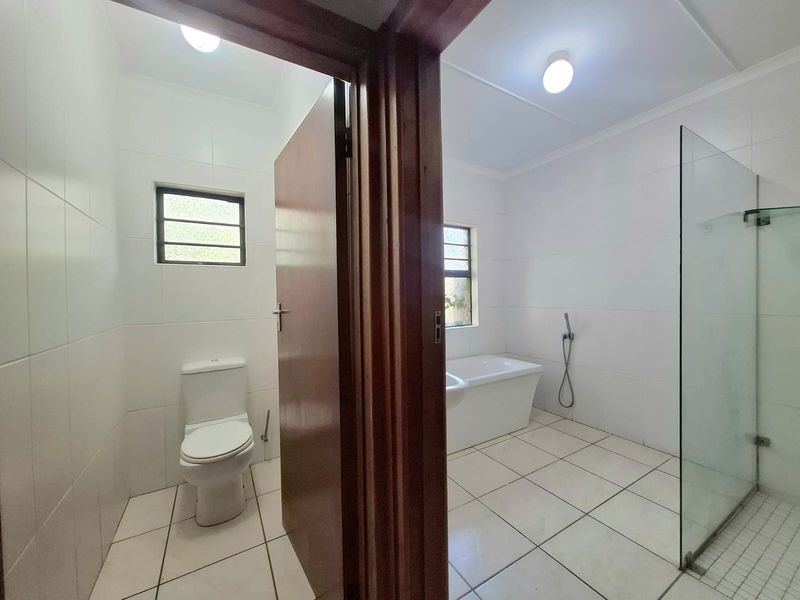 A clean, bright bathroom featuring a separate toilet area, a freestanding bathtub, and a walk-in shower with a glass screen.