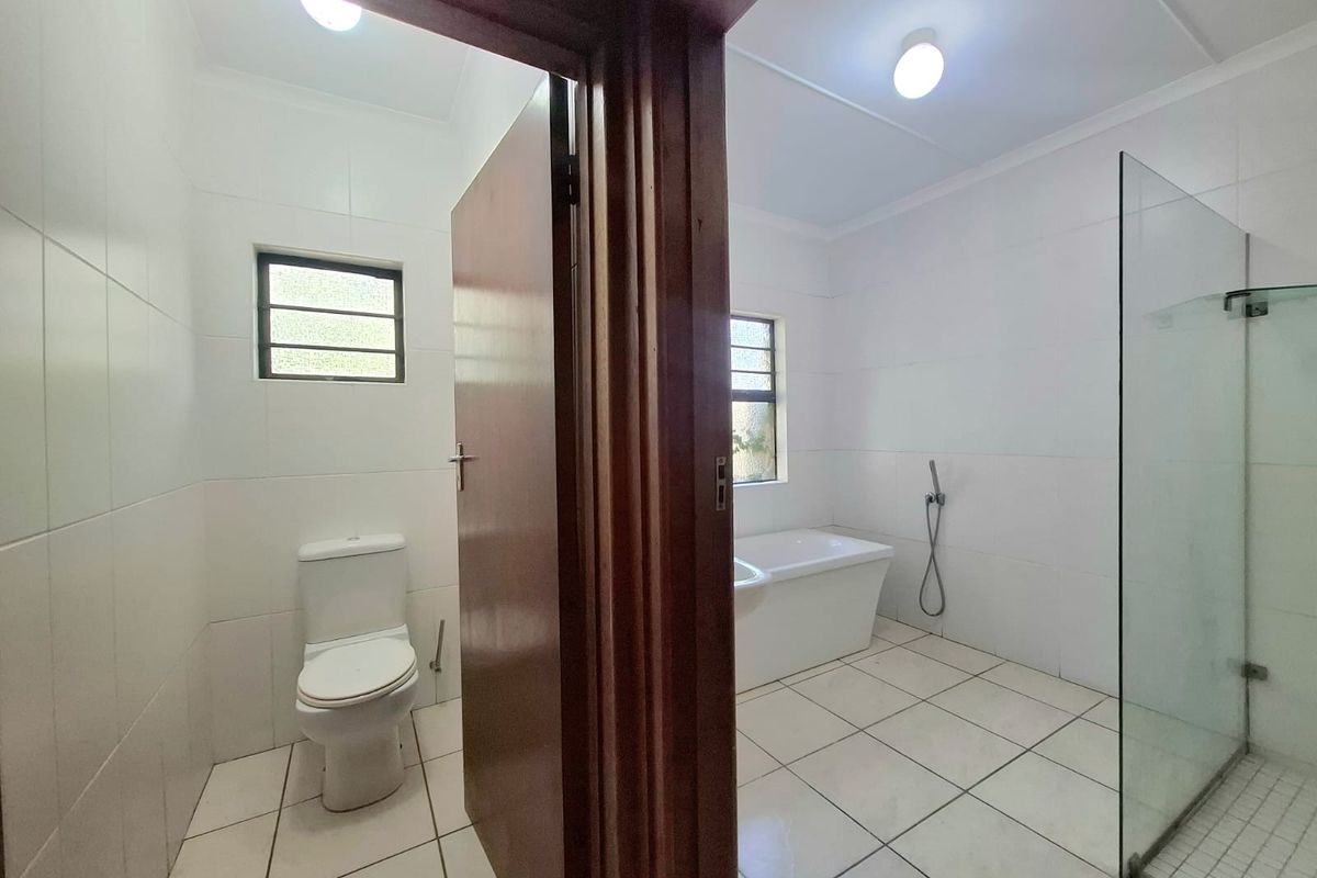 A clean, bright bathroom featuring a separate toilet area, a freestanding bathtub, and a walk-in shower with a glass screen.