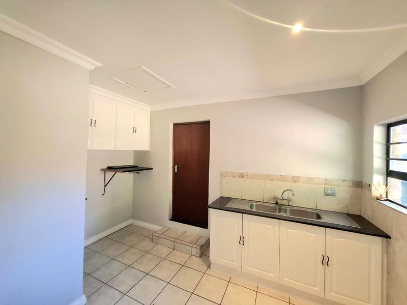 A clean and functional laundry room featuring built-in white cabinetry, a double sink with tiled backsplash, and durable tiled flooring.