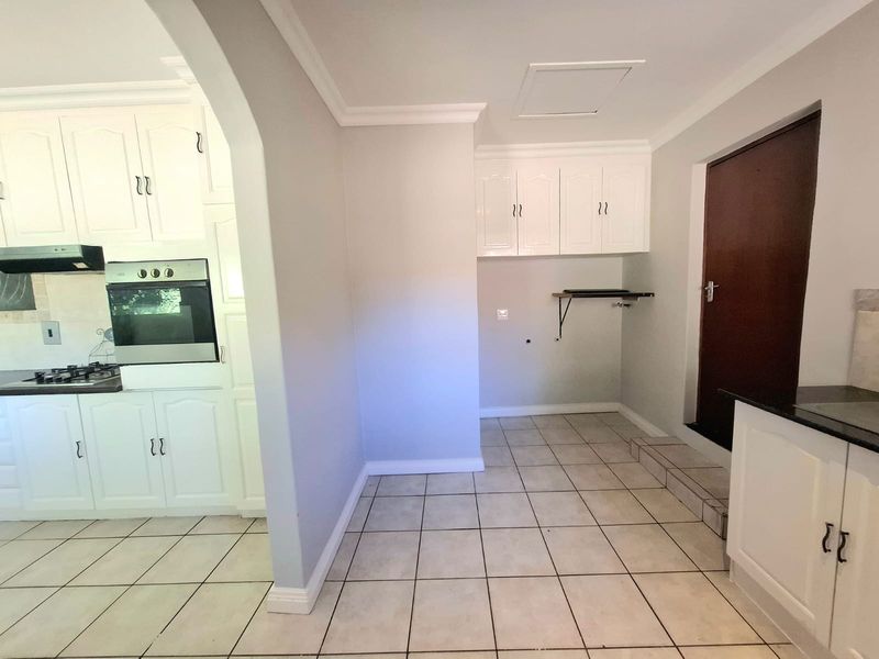 A functional scullery area featuring white built-in cabinetry, tiled flooring, and integrated kitchen appliances, providing additional prep and storage space adjacent to the main kitchen.