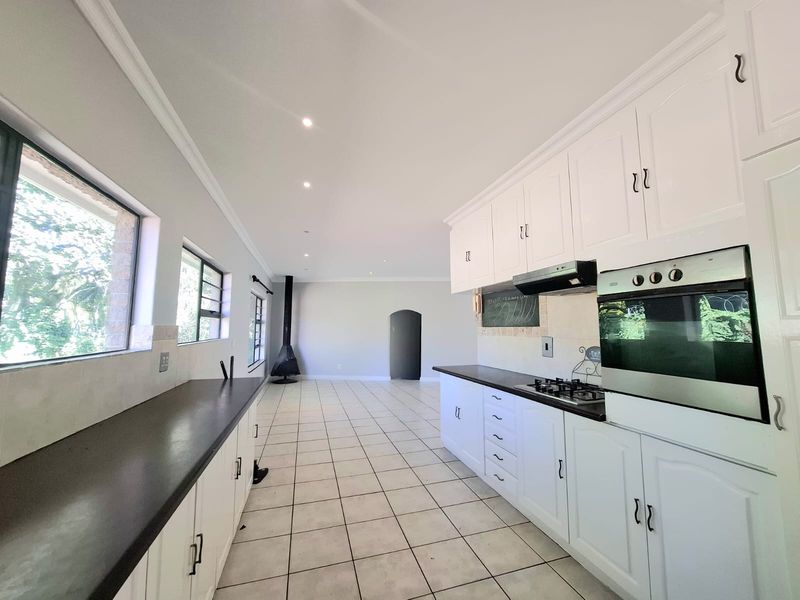 Spacious open-plan kitchen and living area featuring white cabinetry, built-in oven, gas hob, tiled flooring, and a modern freestanding fireplace.