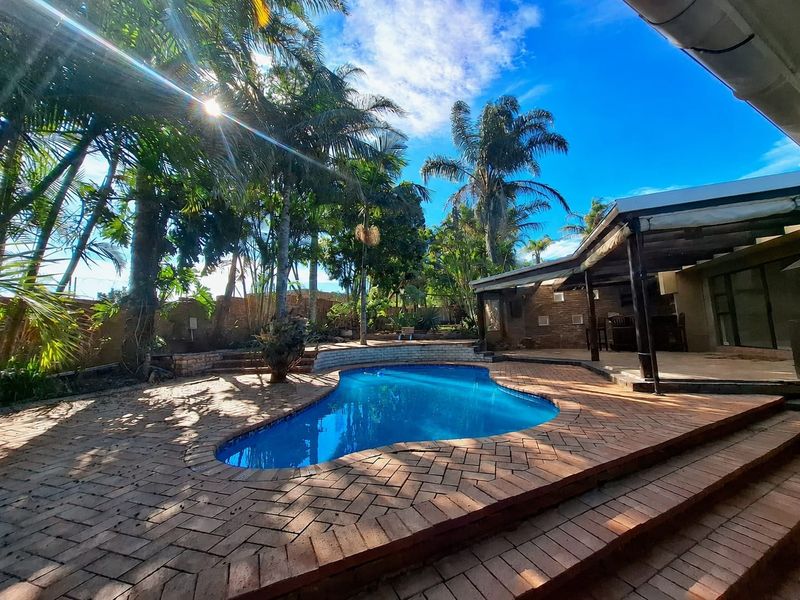 Outdoor pool area featuring a kidney-shaped swimming pool, brick paved surround, and a covered patio area set within a landscaped garden.
