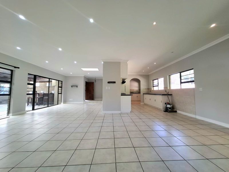 Spacious open-plan living and kitchen area featuring neutral tiled floors, recessed lighting, a skylight, and direct access to an outdoor patio through sliding doors.