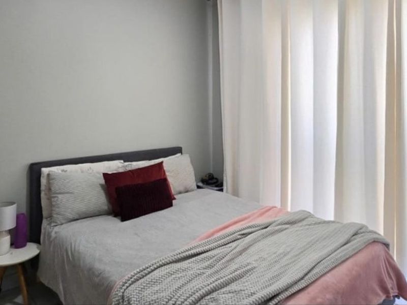 A well-lit bedroom featuring neutral wall tones and floor-to-ceiling curtains, providing a comfortable and private sleeping space.