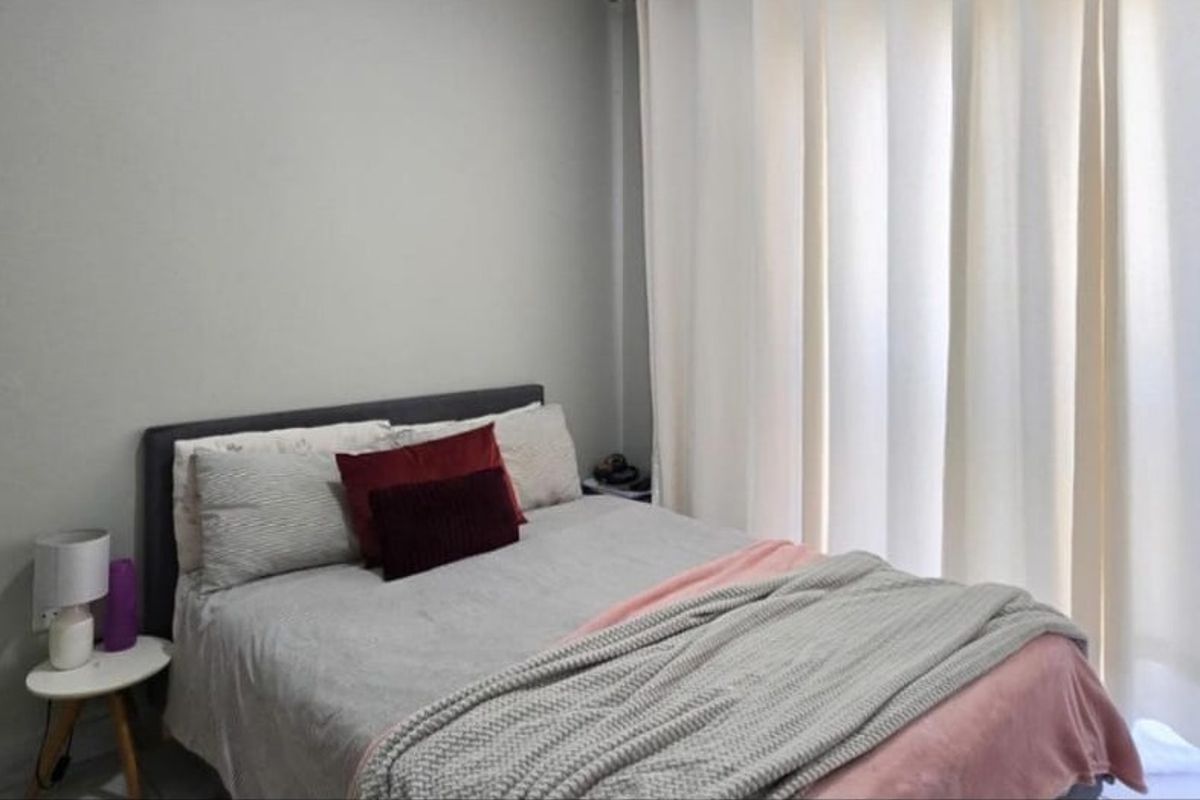A well-lit bedroom featuring neutral wall tones and floor-to-ceiling curtains, providing a comfortable and private sleeping space.