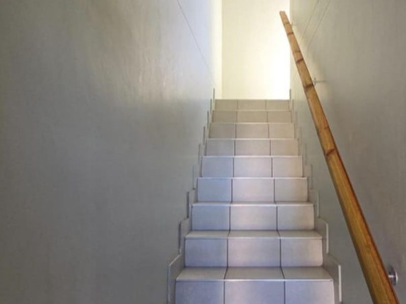 A simple interior staircase featuring tiled steps and a wooden handrail leading to an upper level.