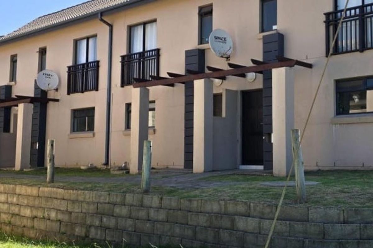 Rear elevation of a multi-story apartment complex featuring ground-level paved patios with pergolas and upper-level balconies.