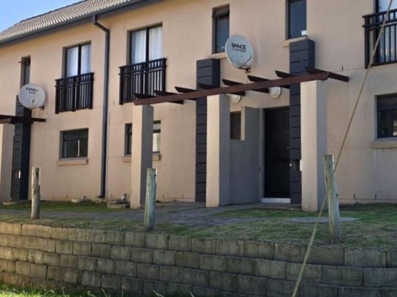 Rear elevation of a multi-story apartment complex featuring ground-level paved patios with pergolas and upper-level balconies.