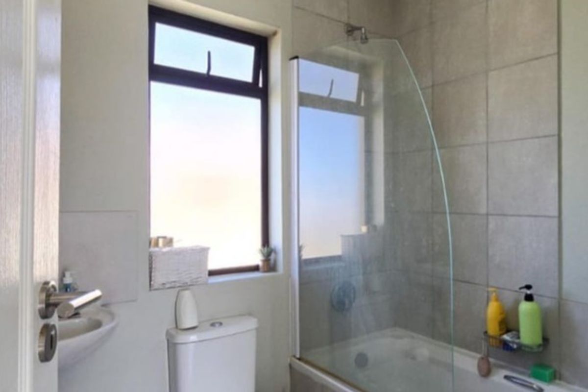 A functional bathroom featuring a bathtub with a glass shower screen, a toilet, and a basin, finished with neutral wall tiling.