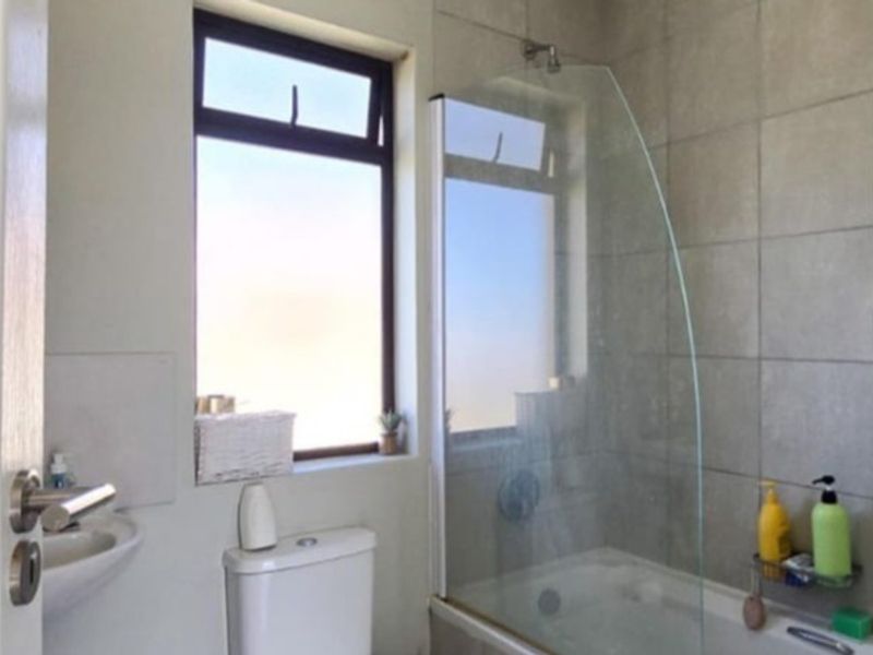 A functional bathroom featuring a bathtub with a glass shower screen, a toilet, and a basin, finished with neutral wall tiling.
