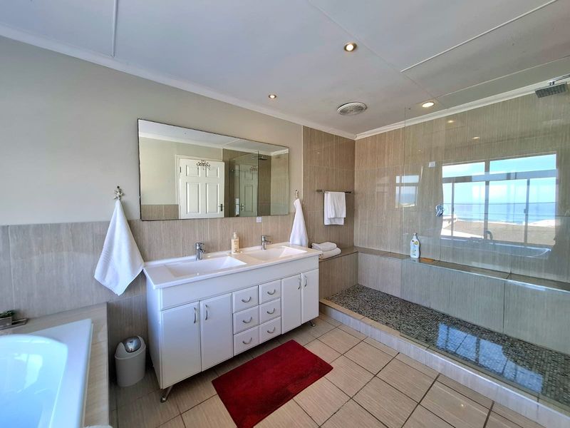 Spacious modern bathroom featuring a double vanity, large wall mirror, and a walk-in shower with glass enclosure and pebble-style floor tiling.