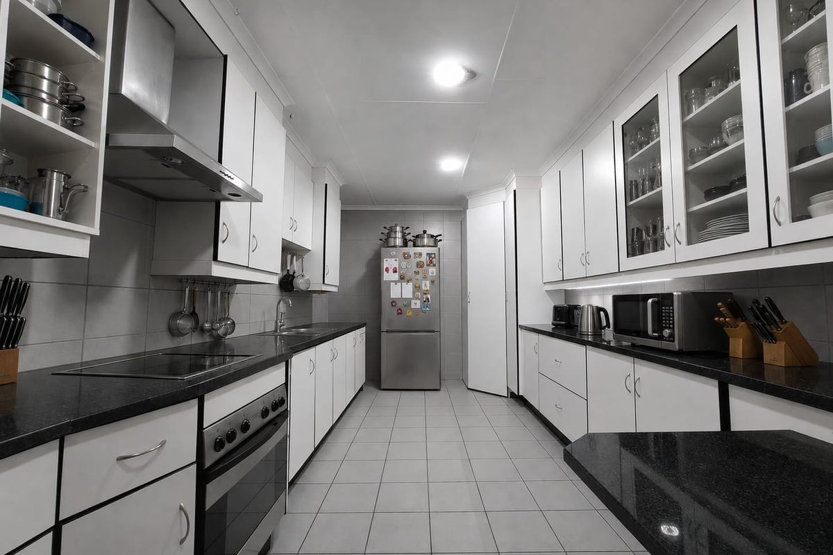 A well-maintained galley-style kitchen featuring white cabinetry, dark granite countertops, stainless steel appliances, and neutral tiled flooring.
