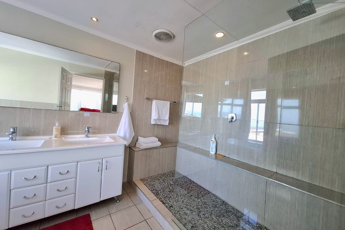 Modern bathroom featuring a double vanity with white cabinetry, a spacious walk-in shower with a rain shower head, and neutral floor-to-ceiling tiling.