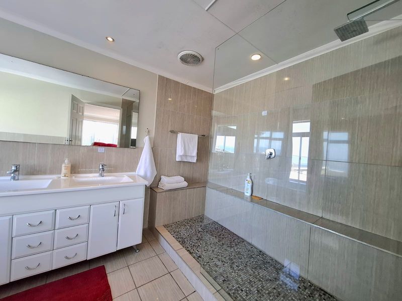 Modern bathroom featuring a double vanity with white cabinetry, a spacious walk-in shower with a rain shower head, and neutral floor-to-ceiling tiling.