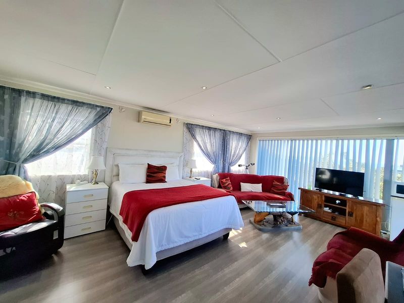 Spacious bedroom featuring laminate flooring, recessed downlighting, and a wall-mounted split-system air conditioner with large windows and vertical blinds.
