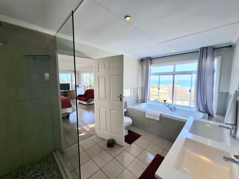 Modern bathroom featuring a glass-enclosed shower, double vanity, and a built-in bathtub positioned to enjoy scenic ocean views.