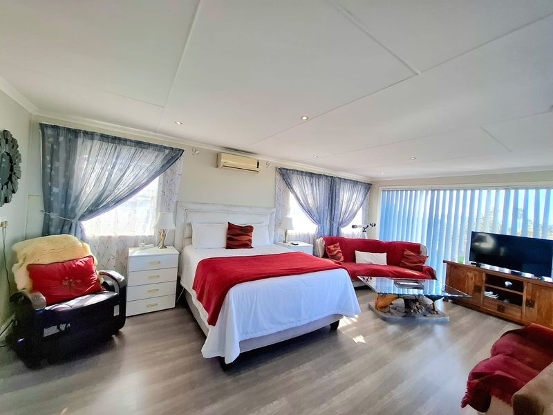 Spacious bedroom featuring laminate flooring, recessed downlighting, and a wall-mounted split-system air conditioner with large windows and vertical blinds.