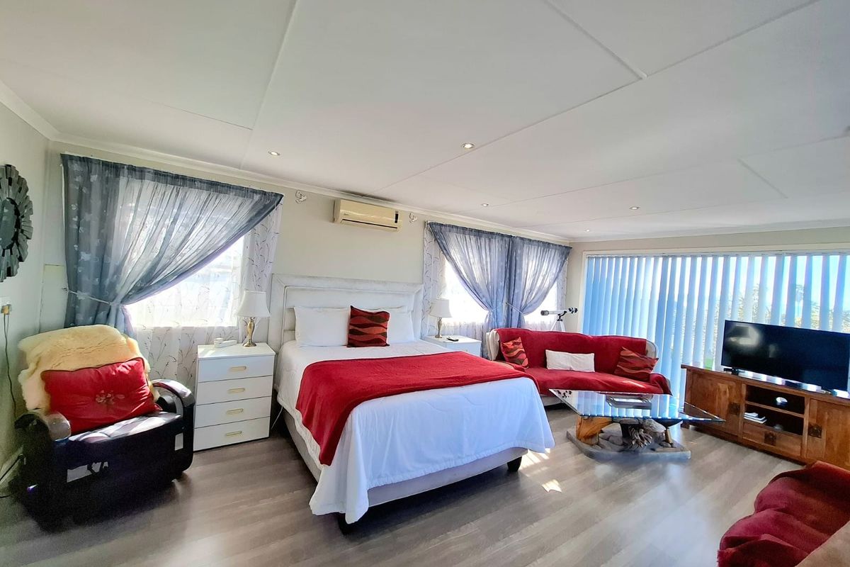 Spacious bedroom featuring laminate flooring, recessed downlighting, and a wall-mounted split-system air conditioner with large windows and vertical blinds.