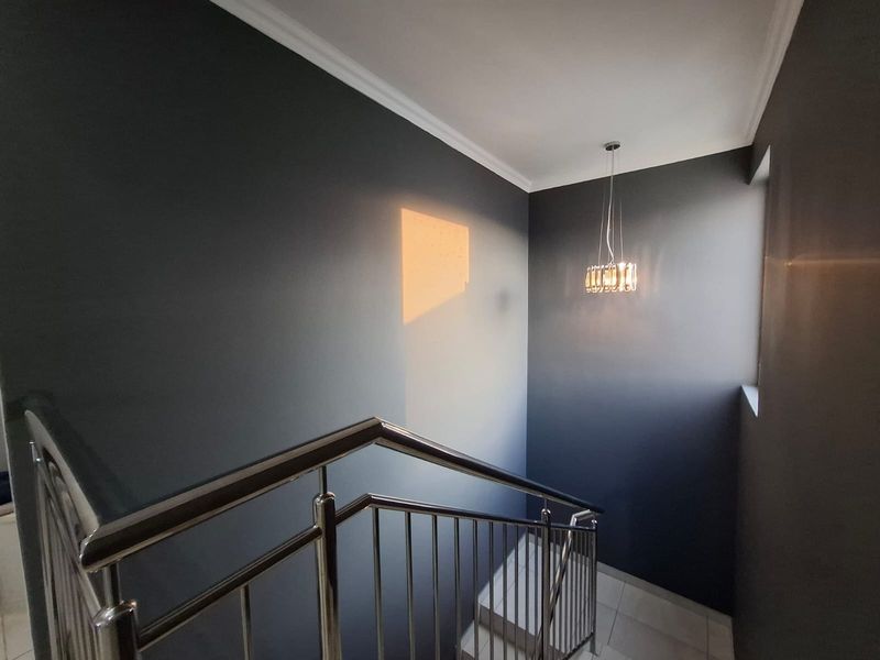 A modern staircase landing featuring dark grey walls, a stainless steel balustrade, and a contemporary pendant light fixture.