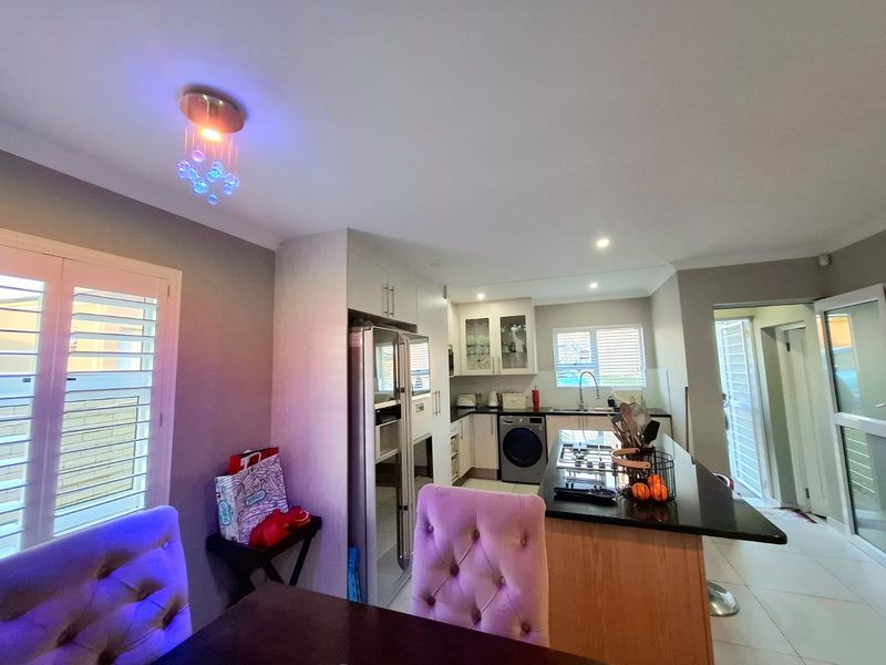 Open-plan kitchen and dining area featuring a central island with granite countertops, modern cabinetry, and integrated appliances, complemented by tiled flooring and shutter blinds.