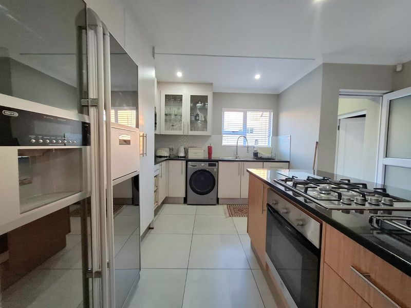 Modern kitchen featuring granite countertops, built-in oven, gas hob, and ample cabinetry with tiled flooring and recessed lighting.