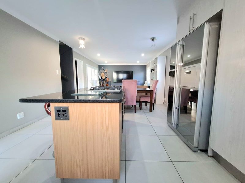 Modern open-plan living area featuring a central kitchen island with gas hob, sleek cabinetry, and large format floor tiles throughout the space.