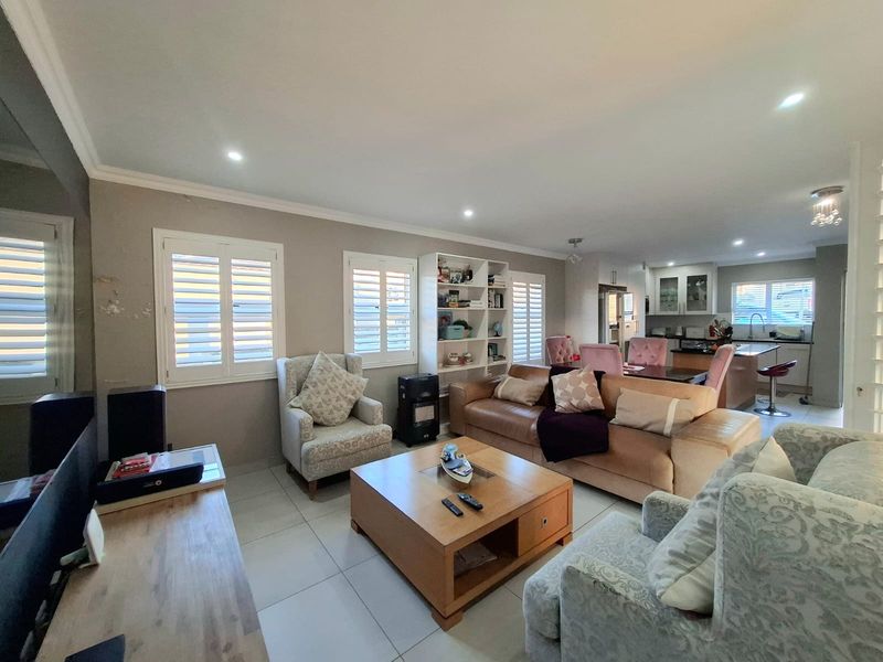 Spacious open-plan living and dining area featuring tiled floors, plantation shutters, built-in shelving, and a functional kitchen with an island.