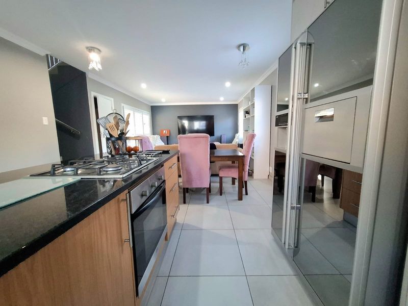 Open-plan living area featuring a modern kitchen with gas cooktop, built-in oven, granite countertops, and tiled flooring, flowing into the dining and lounge space.