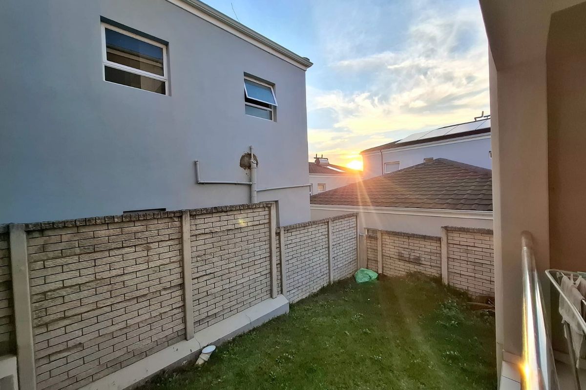 A view of the rear garden area featuring a brick boundary wall, lawn, and exterior building facade with casement windows.