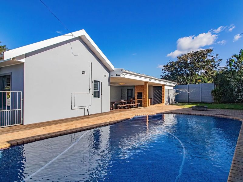 A well-maintained outdoor area featuring a swimming pool, wooden decking, and a covered patio with a built-in braai, perfect for outdoor entertaining.