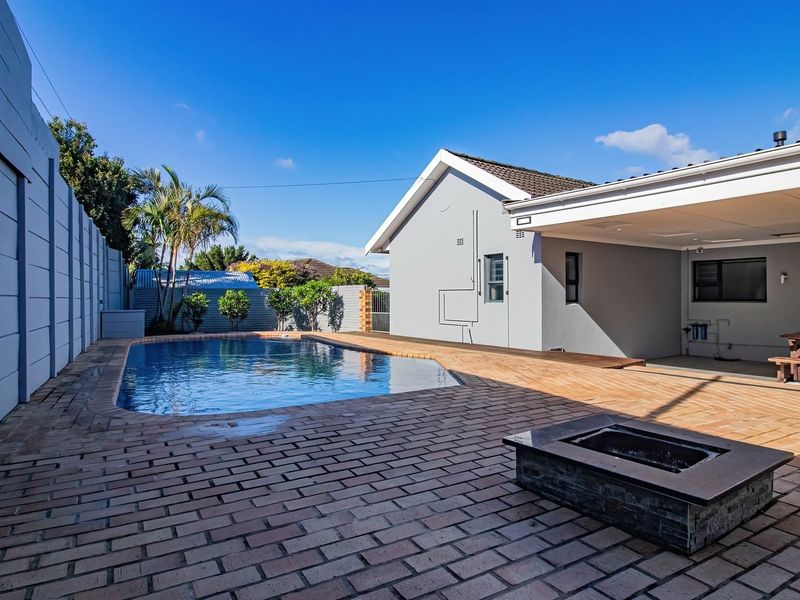 Outdoor entertainment area featuring a swimming pool, brick-paved patio, and a built-in fire pit, set against a well-maintained rear garden and covered patio space.