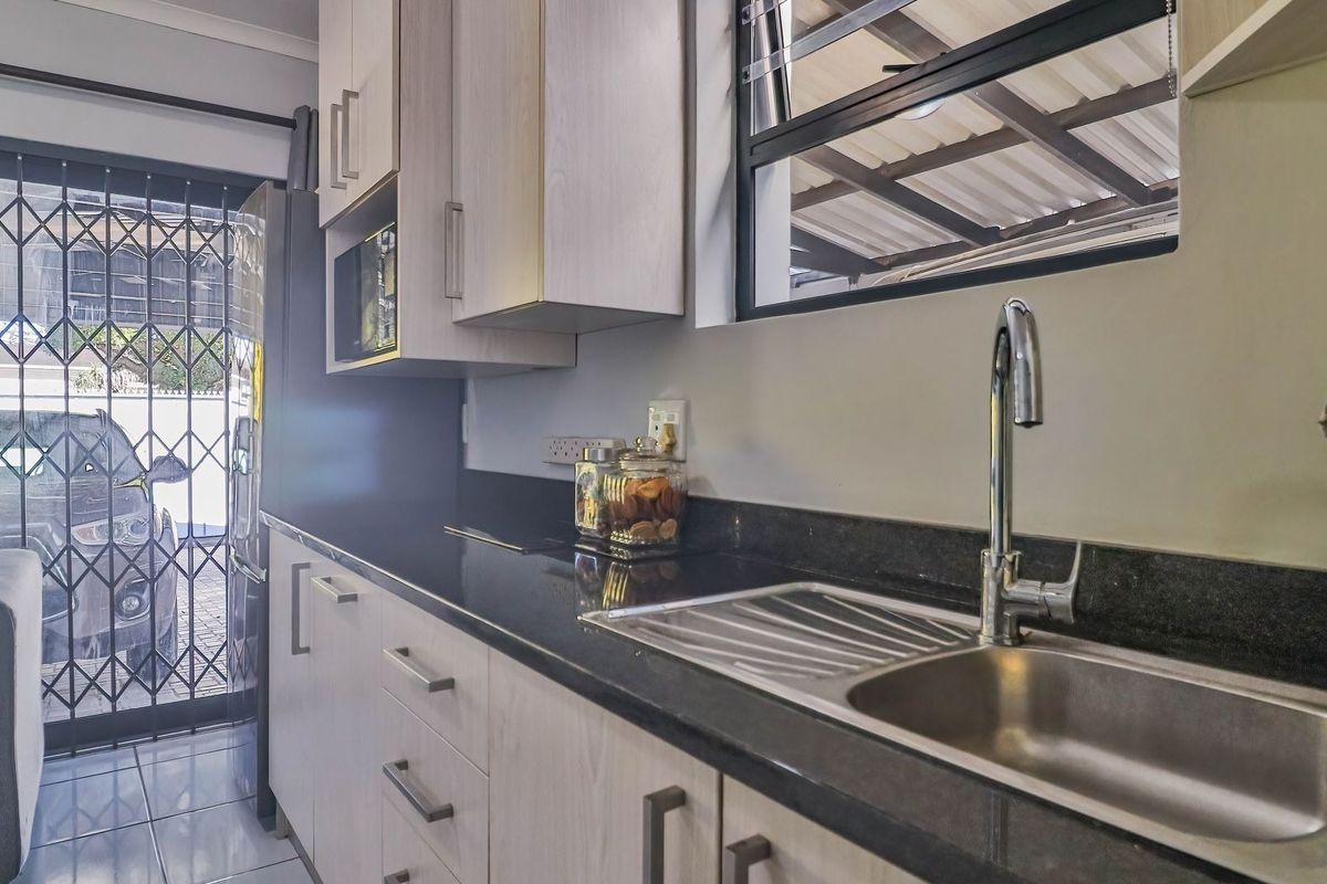 A functional kitchen featuring light-toned cabinetry, dark granite countertops, a stainless steel sink, and direct access to an exterior security gate.