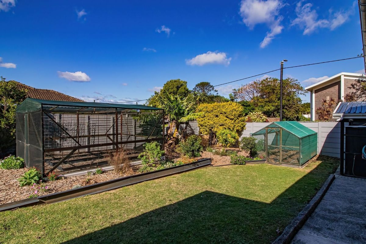 A rear garden area featuring a lawn, concrete pathway, drainage channel, and boundary wall, providing a functional outdoor space.