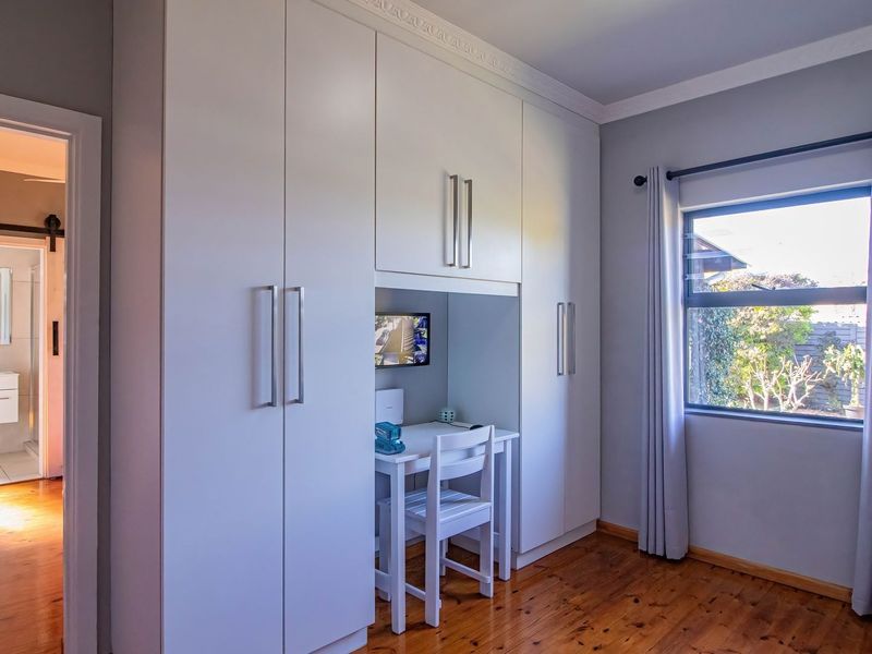A well-maintained bedroom featuring built-in cupboards with an integrated desk space, polished timber flooring, and a view through an aluminium-framed window.