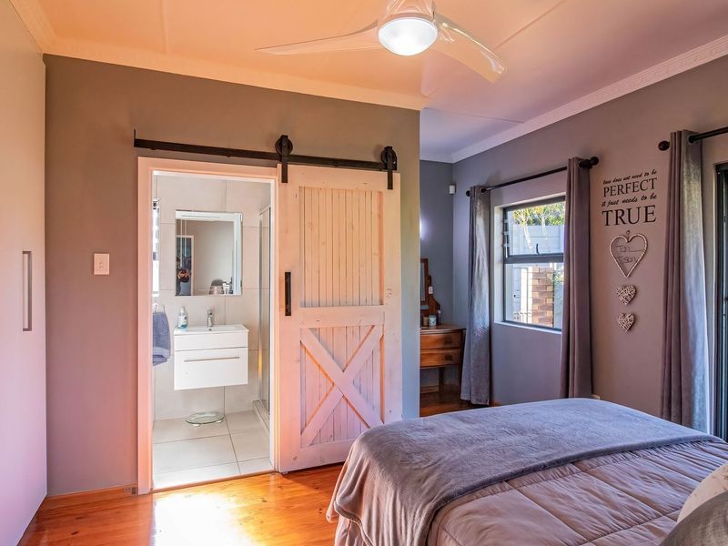 A well-maintained bedroom featuring timber flooring, built-in cupboards, a ceiling fan, and a sliding barn door leading to an en-suite bathroom.