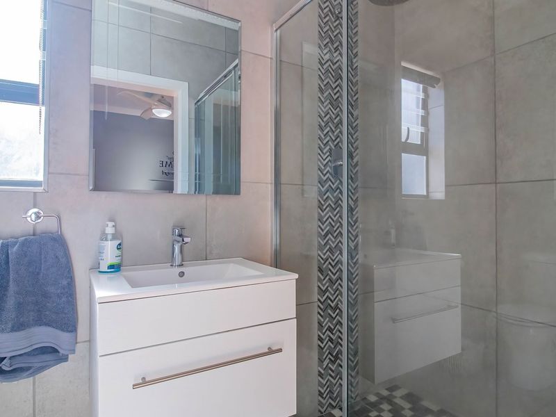 Modern bathroom featuring a sleek vanity cabinet, basin, wall mirror, and a glass-enclosed shower with decorative tiled accents.