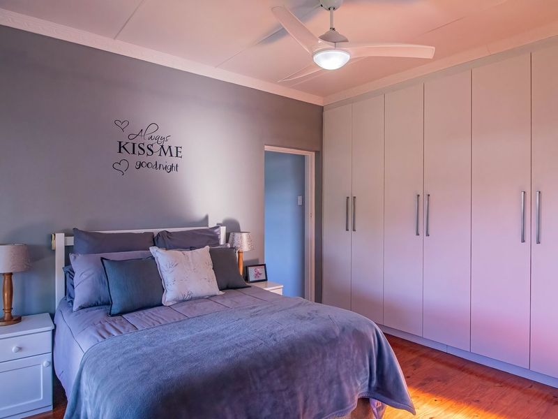A well-maintained bedroom featuring polished hardwood flooring, extensive built-in cabinetry, and a modern ceiling fan.