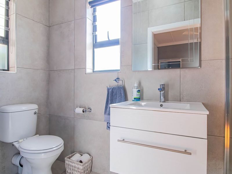 Modern bathroom featuring large format wall tiles, a sleek white vanity with integrated basin, and a glass-enclosed shower area.