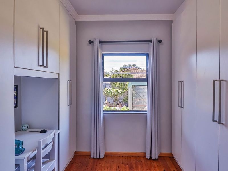 A well-maintained bedroom featuring extensive built-in cabinetry, a integrated desk workspace, timber flooring, and a window with garden views.