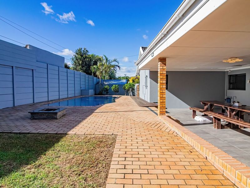 A well-maintained outdoor entertainment area featuring a swimming pool, paved patio, and a covered veranda with tiled flooring.