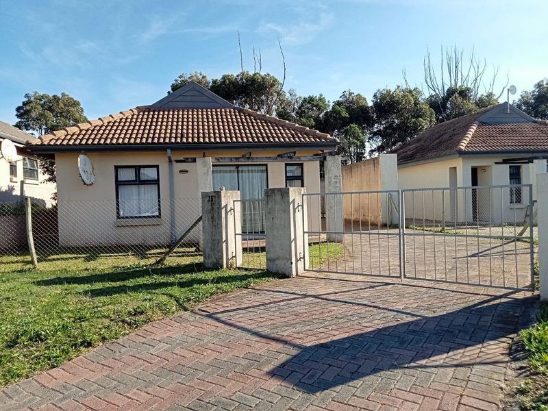 Front view of a cluster home featuring a paved driveway, metal gate, tiled roof, and a sliding glass door entrance.