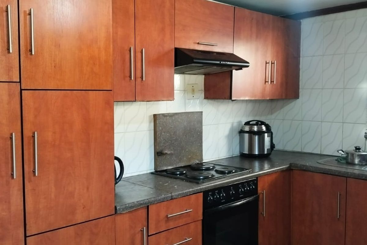 A functional kitchen featuring wood-finish cabinetry, integrated electric hob and oven, extractor fan, and tiled backsplash with a stainless steel sink.