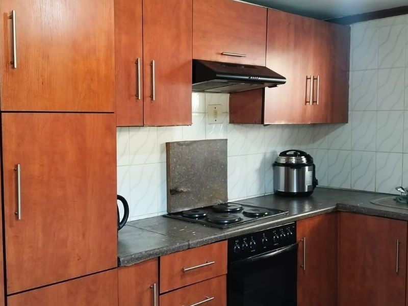 A functional kitchen featuring wood-finish cabinetry, integrated electric hob and oven, extractor fan, and tiled backsplash with a stainless steel sink.