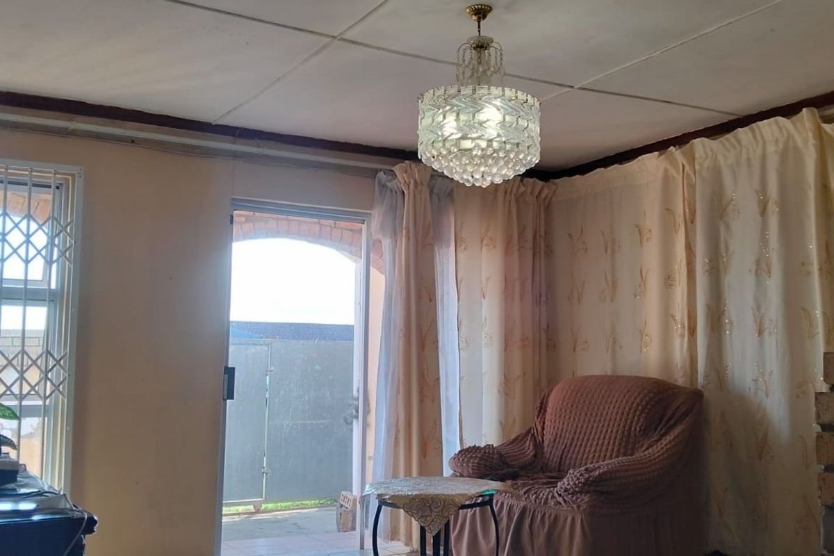 A living room featuring a brick fireplace, crystal chandelier, and direct access to an outdoor area through a sliding glass door with security gate.