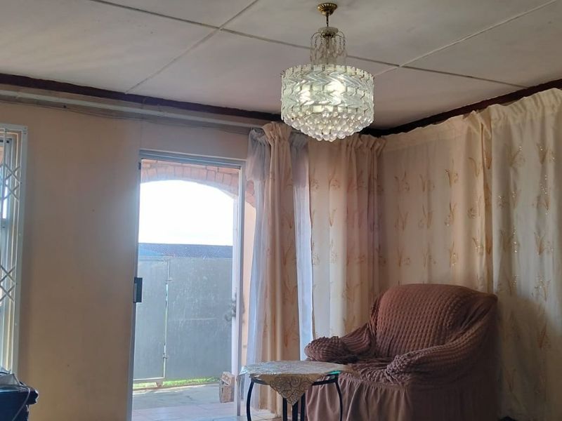 A living room featuring a brick fireplace, crystal chandelier, and direct access to an outdoor area through a sliding glass door with security gate.