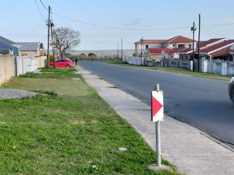 A view of the residential street showing the paved sidewalk, road infrastructure, and surrounding neighborhood boundary walls.