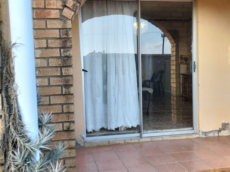 Covered patio area featuring a brick archway, tiled flooring, and a sliding glass door entrance to the home interior.