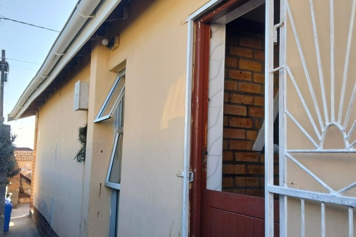 A side view of the property exterior featuring a security gate, aluminium window, and exposed brickwork detail.