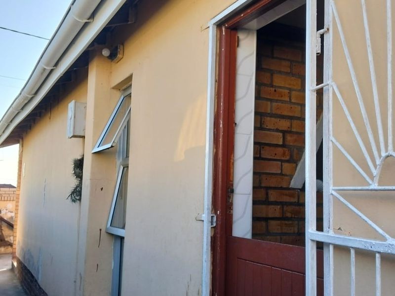 A side view of the property exterior featuring a security gate, aluminium window, and exposed brickwork detail.