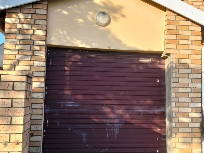 Exterior view of a single garage featuring a brick facade and a roller door in need of maintenance and repainting.